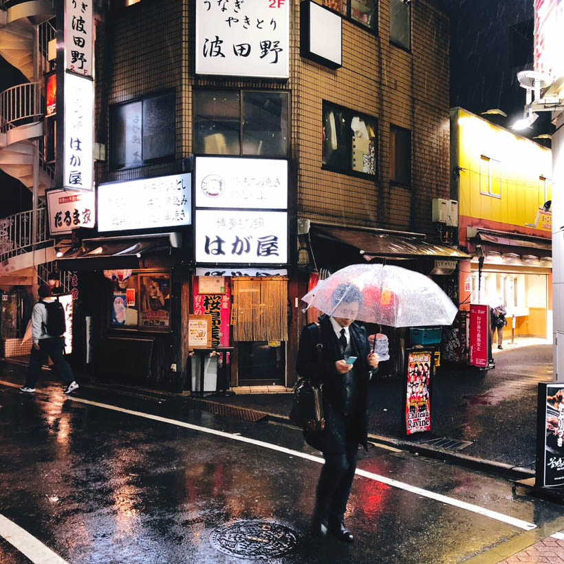 A business man walking in a side street of Shibuya with a transparent umbrella in Tokyo, Japan.