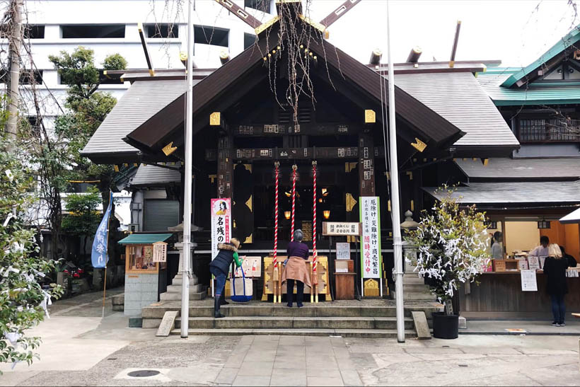 A woman praying and another woman taking pictures at the Namiyoke Inari Shrine, south of Tsukiji Fish Market in Tokyo, Japan.
