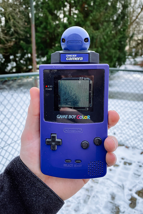 A Game Boy Color with a Game Boy Camera inserted, with the lens pointing at trees in a park in Leuven, Belgium.
