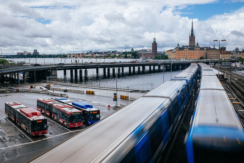 Metro trains between Söderström and Gamla Stan in Stockholm, moving over a bridge that runs over a bus stop.