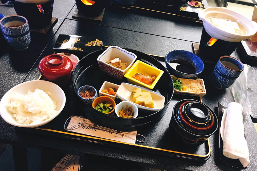 A breakfast meal in a ryokan in Kyoto, Japan: salmon, rice, eggs, ginger, natto, tofu (in a hotpot) and miso soup.