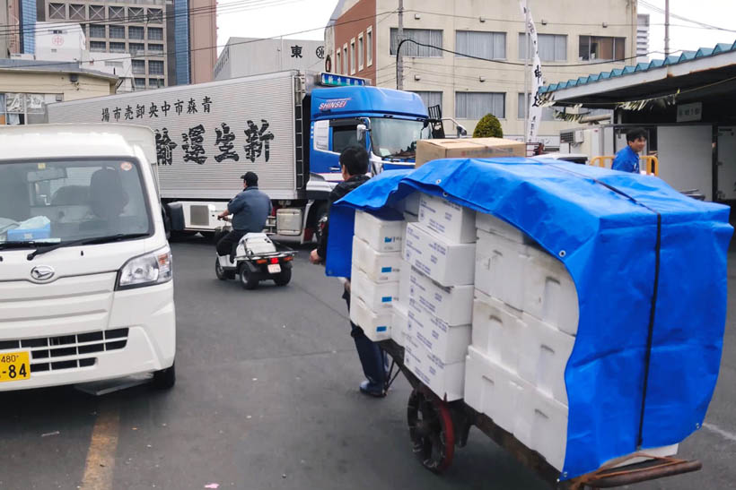 A worker carrying a cart with foam cooling boxes and a blue tarp at Tsukiji Fish Market in Tokyo, Japan.